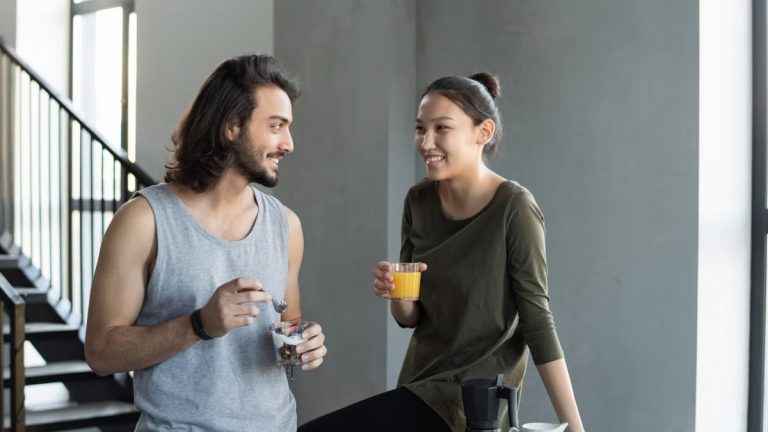 A happy young couple sharing a breakfast moment with juice and snacks indoors.